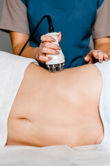 Skin and body care. Woman receives an electric massage against cellulite. Close-up of the apparatus massages belly and legs of woman.