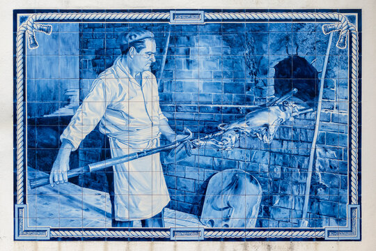  painel de azulejo, num muro público, com a imagem de um homem a assar leitão à bairrada