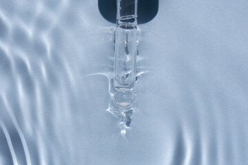 Obraz na płótnie Canvas close up of face serum pipette in a fluid with glare on blue background
