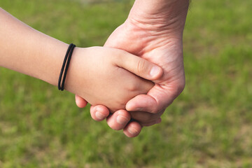 Father holds the hand of a child daughter against blurred nature outdoor background. Trust, care and parenting family, father's day concept