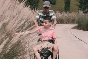 Tuinposter Disabled child sitting on wheel​chair​ and father have fun with activity on the outdoor park on travel, Lifestyle in education age of disabled children, Happy disability kid concept. © GAYSORN