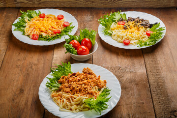 Three plates with different pasta on a wooden table near salted tomatoes.