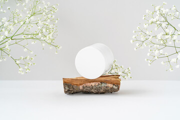 White round blank cosmetic container for branding on rough wooden podium and gentle gypsophila flowers on grey background. Natural cosmetic concept. Beauty product presentation mockup. Copy space. 