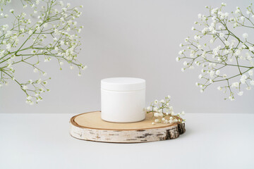 White round blank cosmetic container mockup on wooden podium and lovely gypsophila flowers on grey...