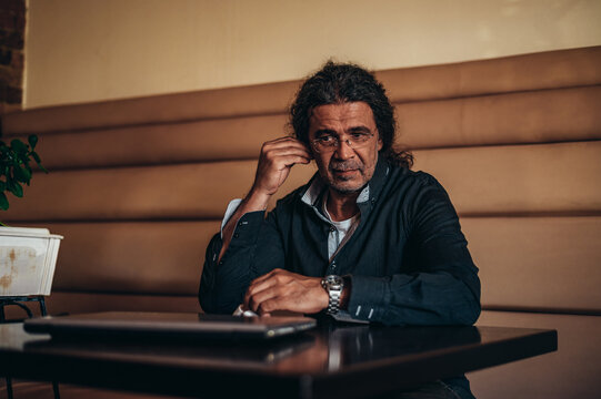 Senior hispanic cuban man putting airpods in his ears in a cafe