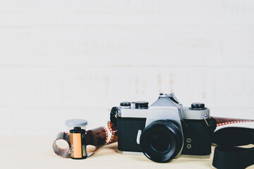 Old 35mm SLR film camera and a roll of film on wooden background. Flim photography concept. - obrazy, fototapety, plakaty