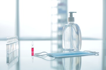 Vial with red and transparent vaccines protective mask and antiseptic on glass table in clinic