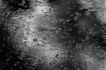 Natural dark background of autumn puddle with drops and circles on water