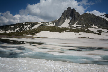 Fototapeta na wymiar Beautiful spring mountain landscape, Rila Mountain, Seven Rila Lakes, Bulgaria. Frozen glacial lakes against the backdrop of a high rocky peak, meadows with blooming crocuses in the foreground.