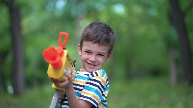 Child boy shoots from toy weapons gun outdoors.