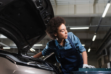 Obraz na płótnie Canvas young african american mechanic fixing car motor in garage
