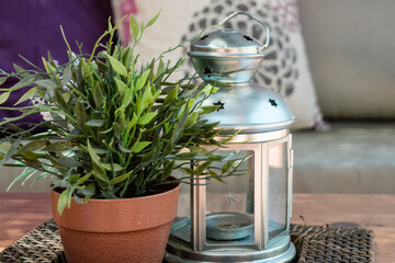 Plant in a pot and tin lantern on a garden table with a background of pillows