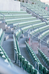 Empty green folding stadium seats in long rows on grey concrete base with grey metal railings
