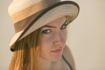 Close-up portrait of an attractive young woman in a summer hat. The girl smiles shyly.