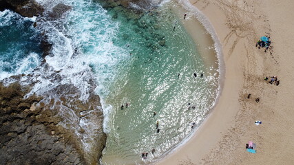 Aerial view of the beach while people swim and walk.