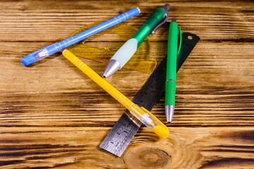 Multi colored ball pens, protractor and ruler on a wooden table