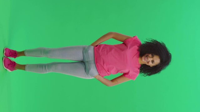Charming cheerful beautiful african american positive woman, gazes happy at camera and enjoying posing on green screen background. Positive feedback, body language concept. Vertical video
