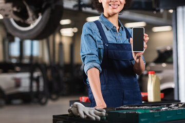 cropped view of young african american mechanic showing cellphone with blank screen in garage