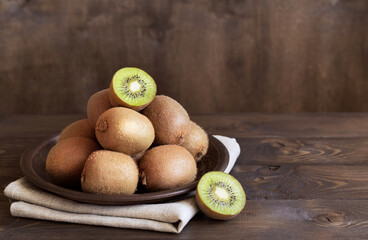 Ripe fresh kiwi fruit in a bowl on a brown wooden background.