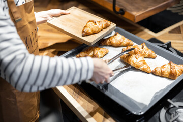 Housewife putting freshly baked croissants on a wooden tray, close-up. Home baking concept