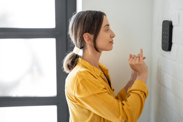 Woman enters a code on the alarm keyboard at the hallway indoors. Concept of home security and...