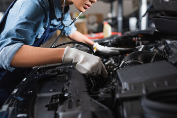 partial view of young african american mechanic in gloves and stethoscope working with car motor in garage