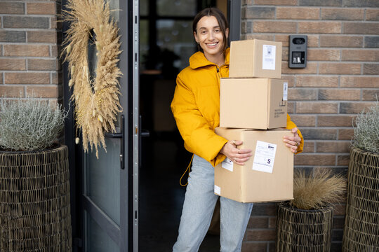 Housewife receiving goods purchased online on the porch of her house, holding cardboard boxes at the entrance door. Concept of contactless food delivery home during a pandemic
