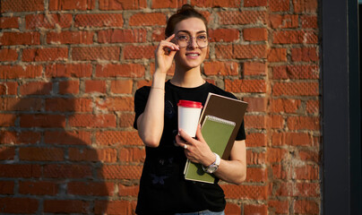 Pensive female student with coffee to go and sketchbook for creating thoughtful looking away in city, contemplative young woman with takeaway caffeine beverage and notepad thinking at street