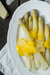 White asparagus with hollandaise sauce, parmesan and lemon zest on white plate on wooden table.