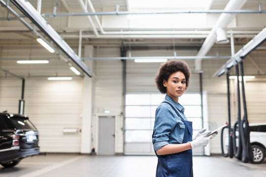 confident young african american mechanic standing with digital tablet and looking at camera in garage