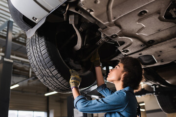 concentrated young african american mechanic working underneath car in garage