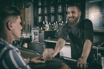Pleasant bartender giving glass of drink to male client