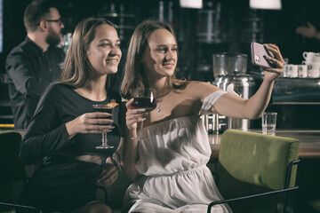 Women taking selfie on mobile while sitting at modern bar
