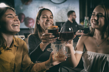 Three women toasting drinks during night party at club