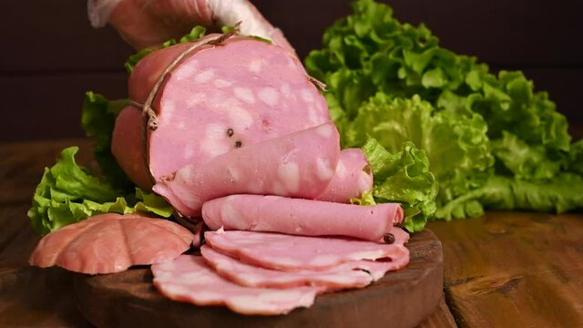 Mortadella. Large mortadella with pistachios on a wooden table. A man cuts thin slices of sausage. Traditional meat food in the Emilia Romagna region in Italy and in the city of Bologna. 4k footage