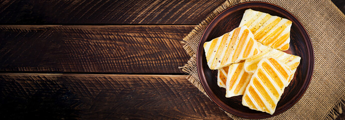 Traditional grilled halloumi cheese on plate on wooden background. Top view, above