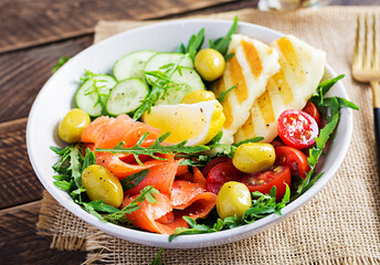 Ketogenic, keto diet. Salted salmon, grilled halloumi cheese, cherry tomatoes and cucumber salad with  olives in white bowl. Healthy food.