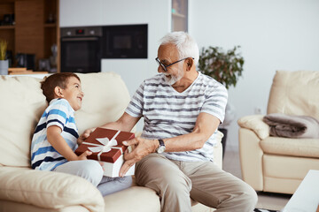 Happy grandfather is having fun with his grandson while opening the gift he received from him.