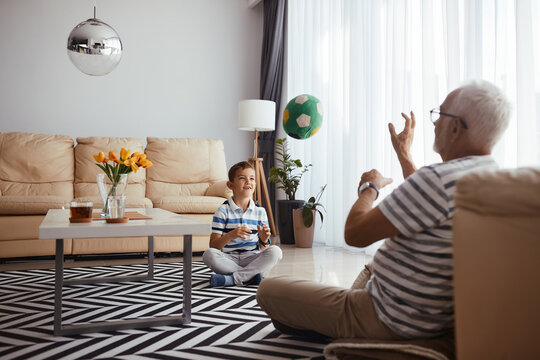 Happy Boy And His Grandfather Playing With A Ball In The Living Room.