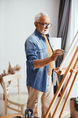 Creative senior man enjoying while painting on canvas at home.