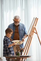 Small boy learning to paint with his grandfather at home.
