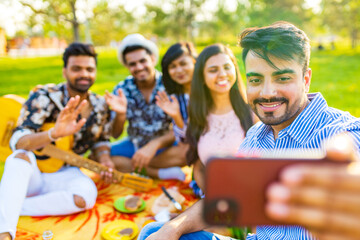 indian students having a lunch and taking selfie on camera phone in Delhi park outdoors