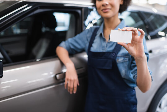 partial view of young african american mechanic showing empty card and standing near car in garage