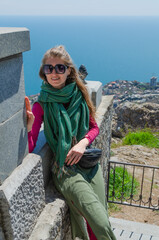 A young woman enjoys the scenic view of the mountains, sea and flowering trees. Spring in the Crimea. Vacation and travel concept.