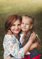 Portrait of a mother and daughter of a preschooler in the summer in the park. A woman hugs her child