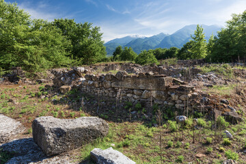 Fototapeta na wymiar Ruins of an ancient Greek stone building at an archaeological site in northern Greece among trees at the foot of a mountain range on a clear sunny day