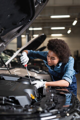 young african american mechanic holding screwdriver and fixing car motor in garage