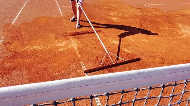 Maintenance of a clay tennis court. Laying a new layer of brick dust, chamotte, and leveling the court surface by hand. Preparing for the new playing season, training and competition.