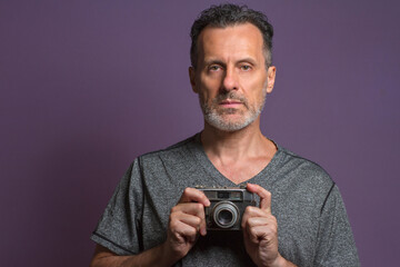 Fototapeta premium Portrait of a professional photographer isolated on a purple background holding a vintage camera in his hands.