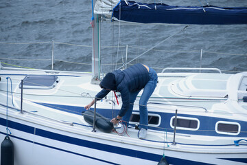 Yachtsman woman stands on a deck of sailing yacht and puts the fenders overboard to moor to a berth